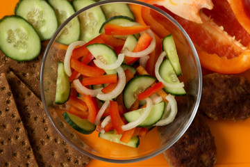 Vegetable salad, meat garnish and bread on an orange background.