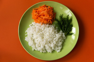 A plate with boiled rice, a side dish of carrots and dill on an orange background.