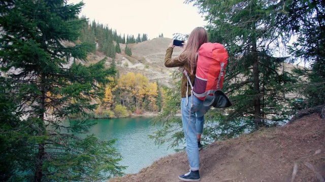 Brave female traveler backpacker capturing freedom picture photo or video by smartphone or mobile phone idyllic stunning pine woods forest mountain lake view in vacations discovering nature check in