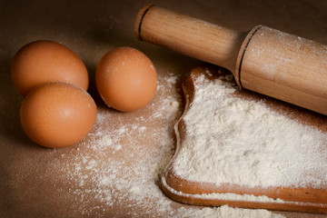 baking ingredients eggs, flour and rolling pin on the table.