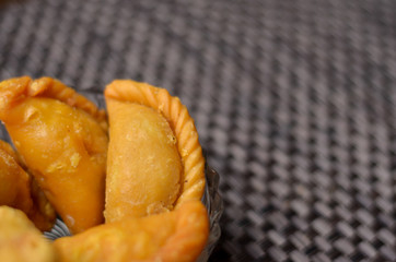 Gujia served in a glass bowl against a brown shiny mat. Is is a popular sweet dish prepared during the festival of Holi  in India