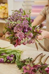 cropped view of woman making bouquet of tulips, peonies and lilac at workplace