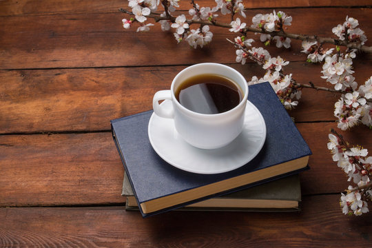Sakura branches with flowers, White cup with Black Coffee and two books on a dark wooden background. Concept of Spring