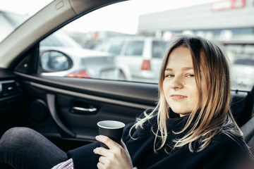 Fototapeta na wymiar cute girl drinks coffee from a plastic cup in a car with leather seats.