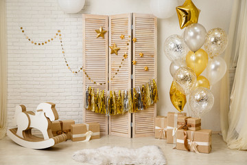 Birthday gold and silver decorations with gifts, toys, garlands and figure for little baby party on a white bricks background.