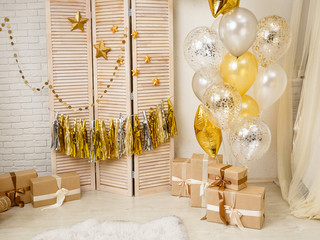 Birthday gold and silver decorations with gifts, toys, garlands and figure for little baby party on a white bricks background.