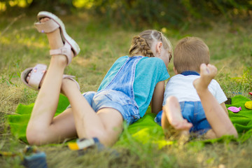 Naklejka na ściany i meble Children lie on summer grass and watch cartoon on phone. Playing games on smart phone. Modern lifestyle and kids concept.