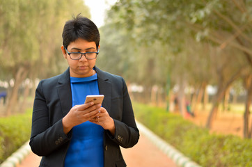 Closeup portrait of a confident young Indian Corporate professional woman with short hair, checking her phone in an outdoor setting wearing a black business / formal suit 