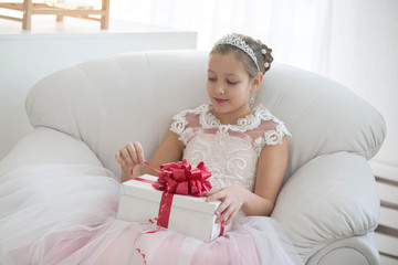 Elegant girl opens a gift.Girl of ten years old with a gift box in a white chair