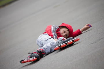 The boy in roller skates lying on the pavement.The child in roller skates fell