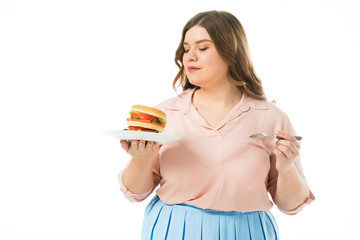 attractive overweight woman looking at tasty burger on plate isolated on white