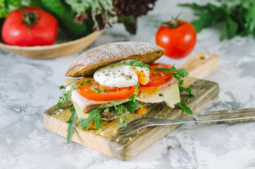 Delicious ciabatta sandwich with ham, tomatoes, arugula and egg poached. Homemade healthy italian sandwich.