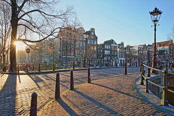 Crooked and colorful heritage buildings along Herengracht Canal and next to Brouwersgracht Canal, Amsterdam, Netherlands. Picture taken at sunrise with a sun star.