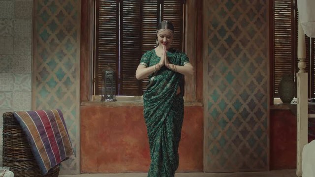 Beautiful female in green sari with bindi point on forehead, many bracelets and tika decoration connecting hands in traditional indian greeting namaste. Smiling woman showing respect and hospitality.