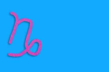 Symbol of astrological sign capricorn cut out of purple paper on blue table. Top view. Horoscope concept. Copy space for your text