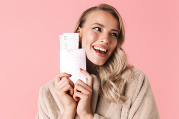 Happy young pretty woman posing isolated over pink wall background holding passport with tickets.