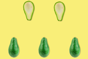 Rows of fresh wholes and halves of organic avocado without kernels in center of yellow table in kitchen or market. Top view. Cooking concept
