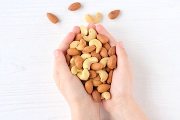 White children hands holding heap of nuts mix with selective focus on blurred background. Almond and cashew nuts in the hands of a child. Roasted almond and cashew nuts. Delicious protein snack