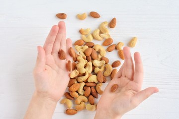 White children hands holding heap of nuts mix with selective focus on blurred background. Almond...