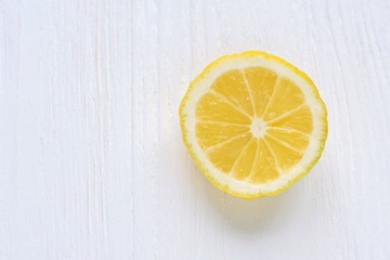 Fototapeta na wymiar slice of juicy yellow lemon with selective focus on white wooden background. Fresh cutting organic lemon on blurred neutral backdrop. Citrus flat lay with empty space for text