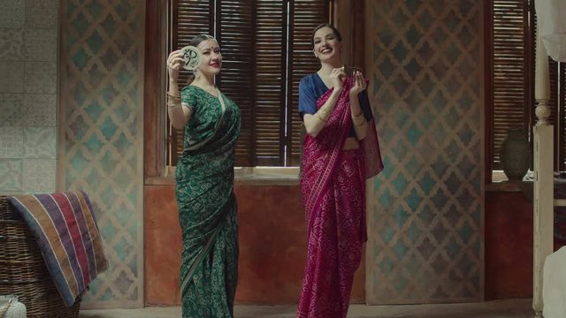 Elegant smiling women in colorful hindu clothing saree, traditional jewelry and bindi points performing flowing dance to meditative music of ethnic indian percussion instruments: karatalas, kanjira.