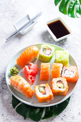 Various sushi on ceramic plate with metal Korean sticks on light stone background with green leaves, flat lay