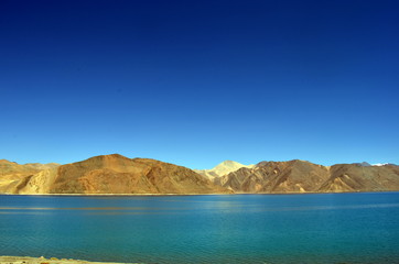 View of Pangong Lake (Tso) from the beachside. The clear blue water stands out amidst skies and...