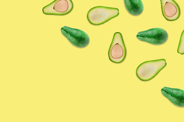 Scattered whole and halves of organic avocado with and without kernels on yellow table in kitchen or market. Top view. Cooking concept. Copy space for your text