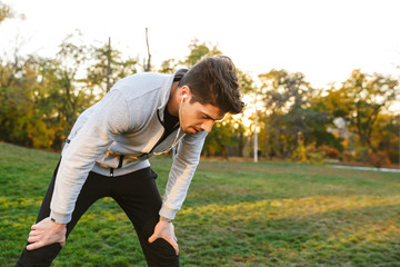 Sportsman outdoors in park listening music with earphones have a rest.