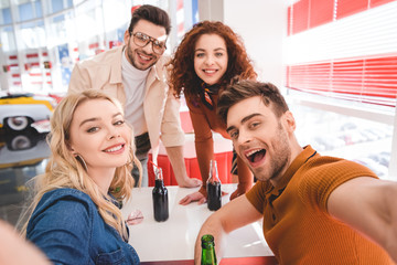 selective focus of smiling  handsome and attractive friends holding glass bottles with soda and beer