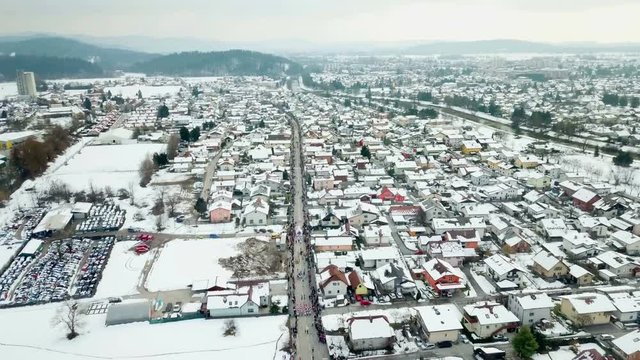 There is a lot of snow in the city when a parade is taking place. Aerial shot. The carnival is going on on a long street.