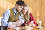 handsome man holding coffee cup and woman using smartphone at cafe