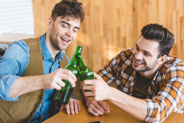 handsome and smiling men cheering with glass bottles of beer