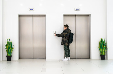 Boy with casual clothes and white sneakers call the elevator. White contemporary building interior.