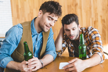 handsome men holding glass bottles of beer and using smartphone