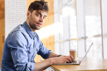 handsome man using laptop and looking at camera at cafe