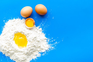 Making dough concept. Pile of flour and eggs on blue background top view copy space