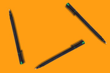 Scattered black and green plastic pens on orange background. Top view