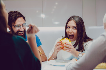 Girl taking a bite of burger while friends are laughing