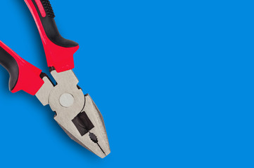 One new metal pliers with rubber handles black and red color on blue table with copy space for your text. Top view. Repair or building concept