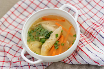 Chicken soup with green onions, on a white chequered table-napkin