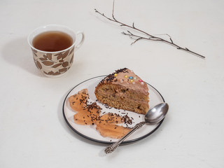 Sweet lunch from homemade cake and tea in a mug with a pattern of leaves on a white background, in the background a dry branch.