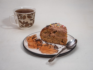 A piece of homemade cake on a small plate and a mug of tea and a pattern of leaves