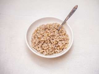 Boiled pearl barley in a deep plate with a spoon on a white background