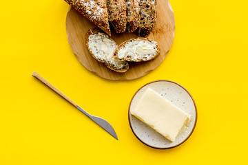 Traditional breakfast. Wholegrain bread on cutting board with butter, slice of bread on yellow background top view
