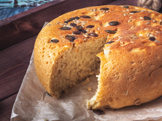 Round-shaped homemade bread with seeds in a cut on a wooden dark tray, closeup shot