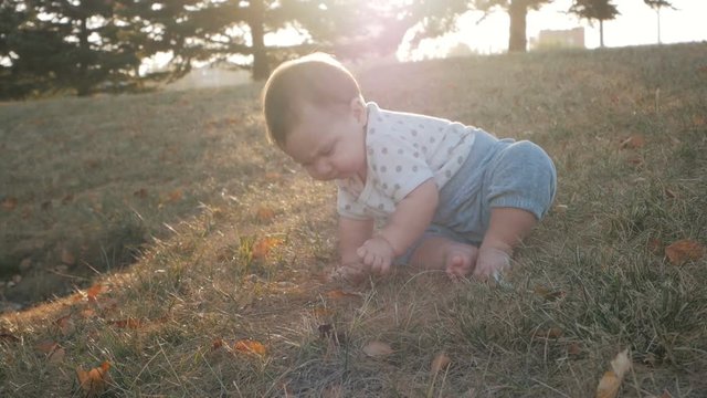 Small baby girl sitting on grass in park. Beautiful baby portrait in nature