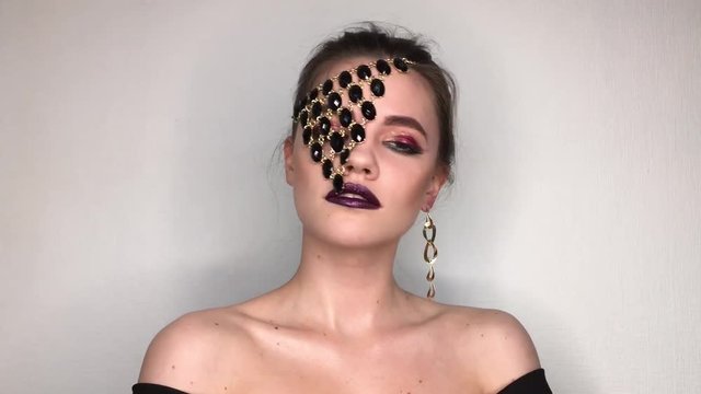 Beauty portrait of a woman with bright colorful make-up and jewellery necklace over one eye