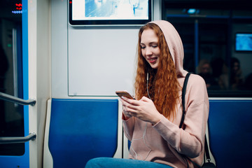 Positive redhead young female with mobile phone in public transport, bus, tram, trolley bus.