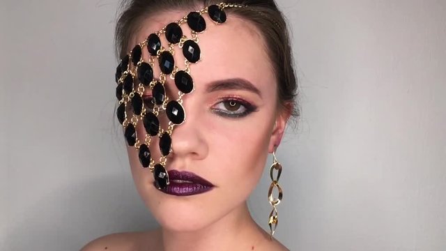 Beauty portrait of a woman with bright colorful make-up and jewellery necklace over one eye
